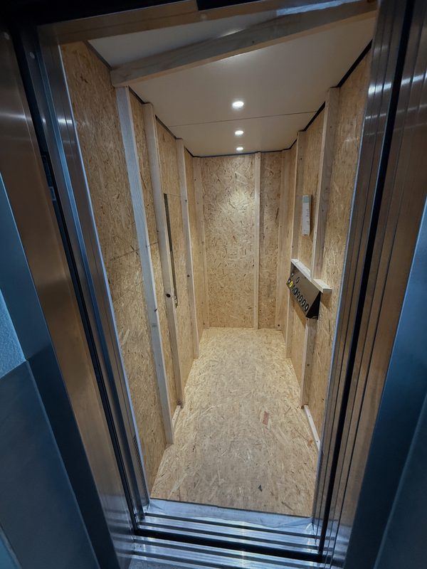 Blick in einen Aufzug, dessen Innenwände für den Transport vollständig mit Holzplatten verkleidet sind