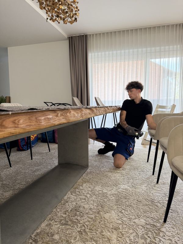 Unter einer Tischplatte kniend verschraubt ein Monteur das Gestell