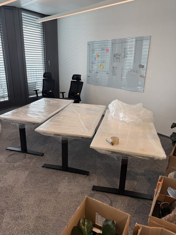Drei höhenverstellbare Schreibtische mit folierten Platten stehen nebeneinander in einem Büro