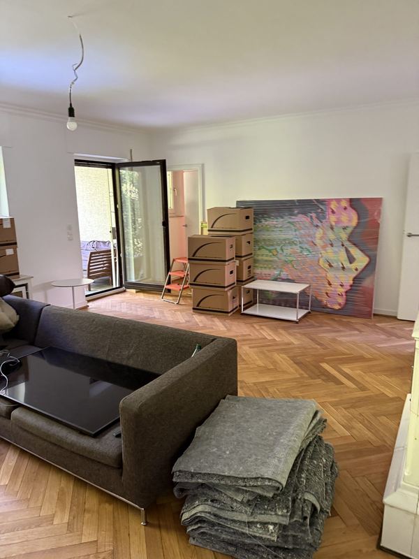 Wohnzimmer mit Kartonstapeln entlang der Wand und gefalteten Umzugsdecken