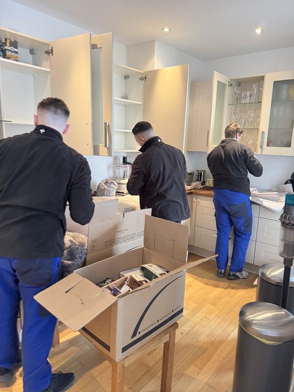 Drei Mitarbeiter leeren Küchenoberschränke und verpacken den Inhalt in Kartons