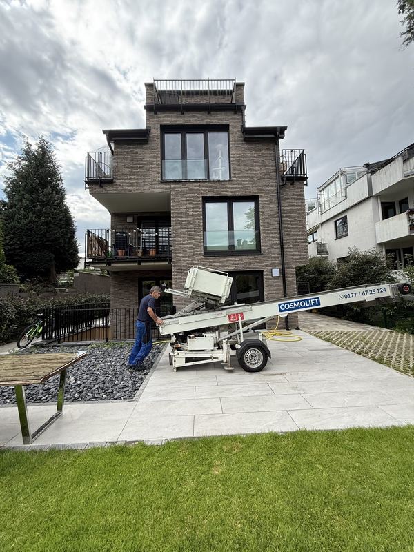 Auf der Einfahrt vor einem Wohnhaus richtet ein Mitarbeiter den Möbellift aus