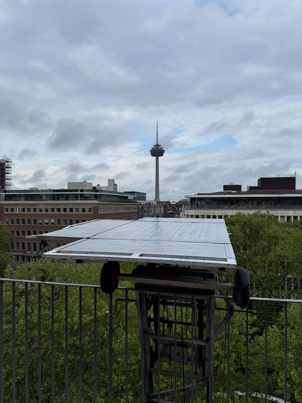 Plattform eines Möbellifts in Höhe eines oberen Stockwerks, dahinter ein Fernsehturm