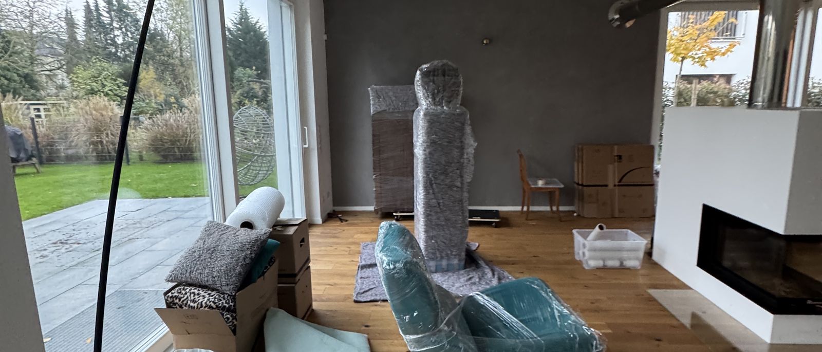 Privatumzug in Bonn: helles Wohnzimmer mit Blick in den Garten, Stehlampe und Möbel sind in Umzugsdecken eingepackt