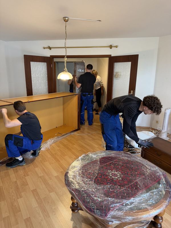 Vier Mitarbeiter heben zusammen den Korpus einer großen Wohnzimmerschrankwand an