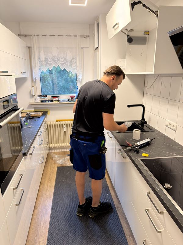 Eine schwarze Spüle wird von einem Mitarbeiter in den Ausschnitt der Arbeitsplatte eingesetzt