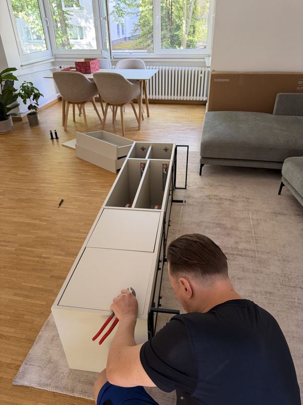 Von oben gesehen: ein Monteur bringt an einem liegenden Sideboard die Beschläge an