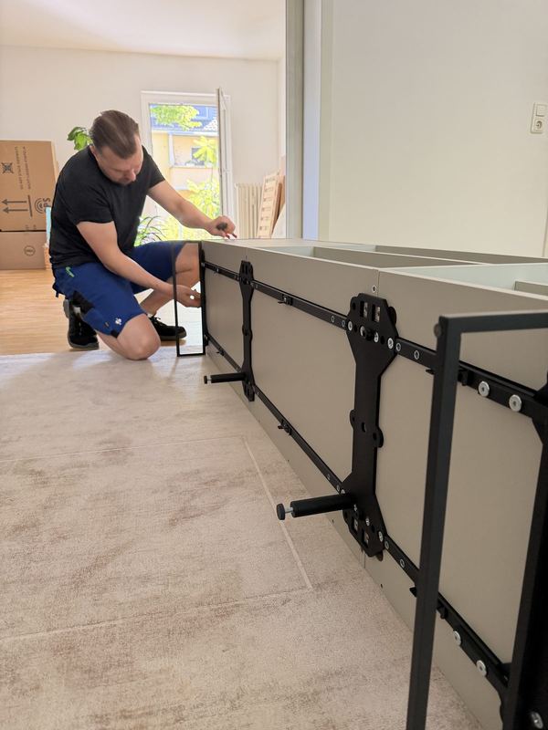 Vor einem liegenden Sideboard kniet ein Mitarbeiter und bringt die Beschläge an