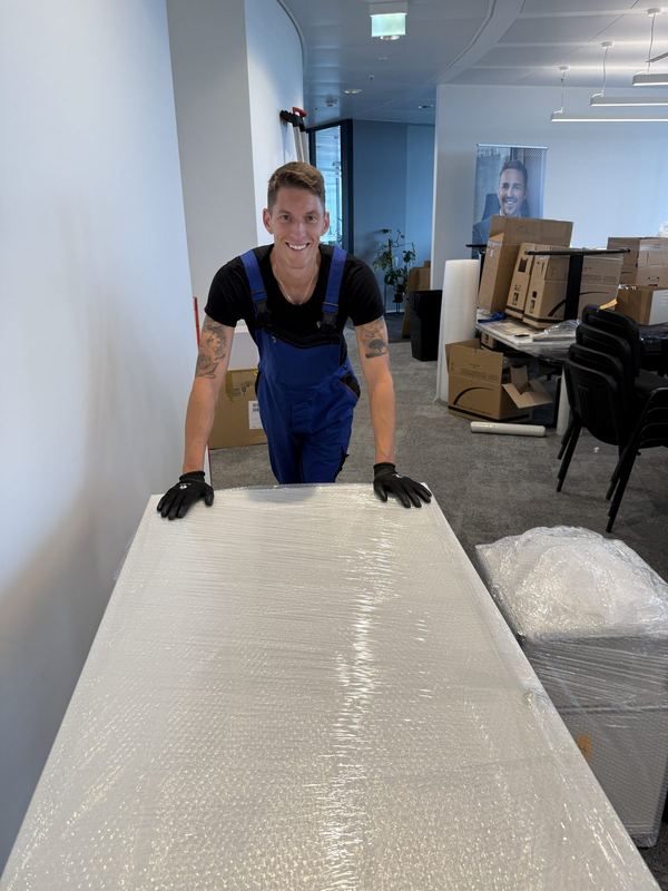 Hinter einer vollflächig mit Luftpolsterfolie verpackten Tischplatte steht ein Mitarbeiter