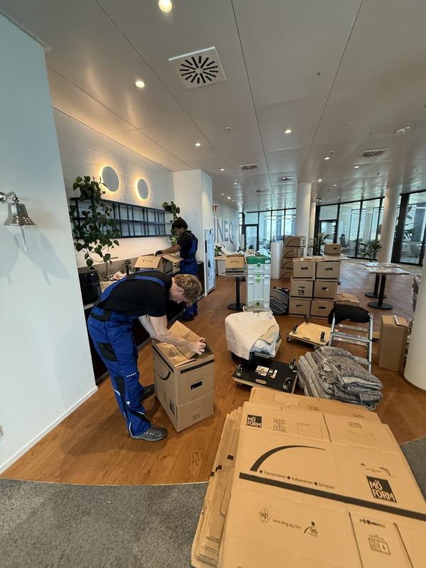 In einem Büro verschließt ein Mitarbeiter einen Umzugskarton, dahinter weitere Kartons